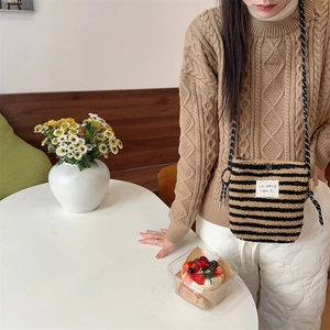 Detail of plush striped crossbody bag featuring a woven label in a cozy cafe setting