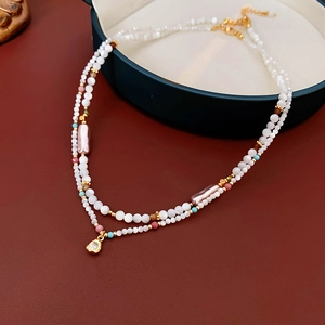 Close-up of double-layered pearl necklace with golden heart pendant on green jewelry box