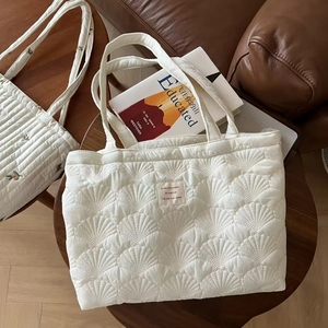 Detail of white quilted tote bag featuring shell stitching and minimalist fabric label