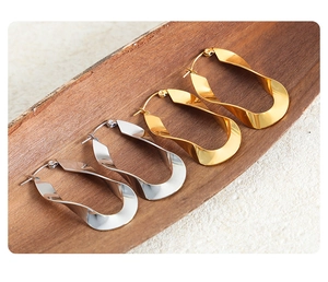 Close-up of gold and silver twisted U-shaped earrings on a dark wooden display