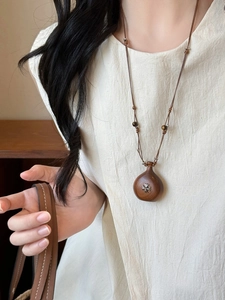 Detail of wooden gourd pendant with metallic cross inlay on a brown cord necklace