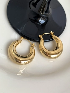Macro view of thick gold polished metal hoop earrings placed on a white ceramic plate