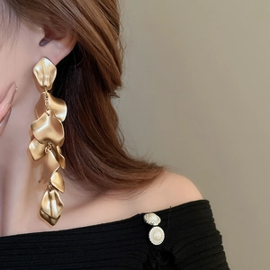 Detailed view of matte gold long pleated petal tassel earrings on model showing drape