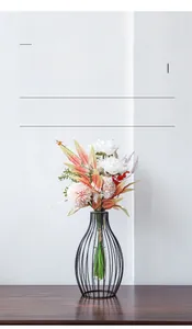 Detail of transparent glass tube vase with faux flowers in black iron lantern frame