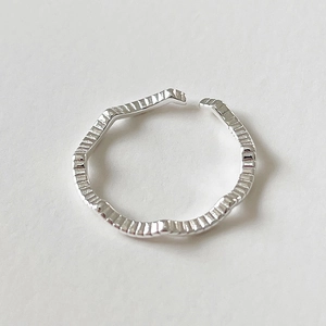 Detailed close-up of a silver wavy open ring with fine vertical texture on a white base