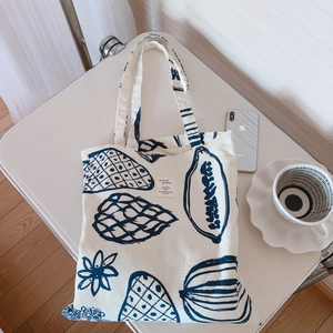 Vue à plat d'un sac cabas en toile blanc cassé avec imprimé bleu sur un bureau blanc