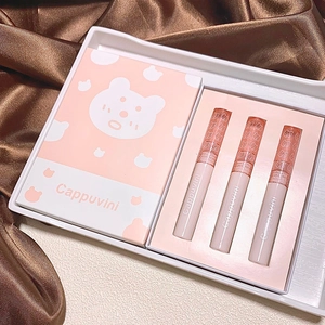 Detailed view of three pink bear-themed lip gloss tubes in a branded gift box on brown silk