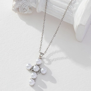 Detailed view of white pearl cross pendant on a thin silver chain over white stone