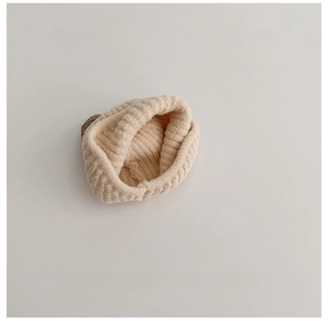 Detail of off-white knitted baby hat with thick ribbed texture and brown leather label