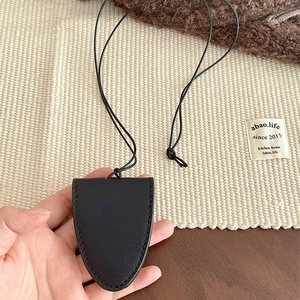 Detail of shield-shaped black leather clochette key holder on minimalist cord strap