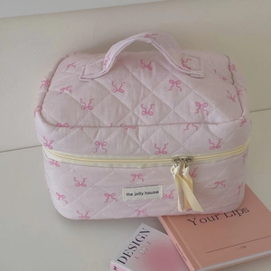 Detail of pink quilted makeup bag with bow prints, top handle, and ribbon zipper pull