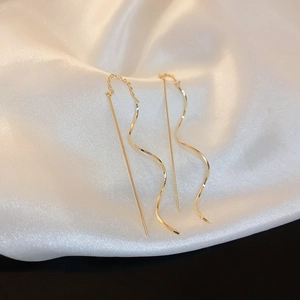 Detailed view of elegant gold wave tassel chain earrings on soft white silk background