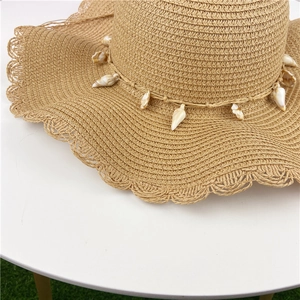Close-up of wavy brim straw hat with decorative seashell band on white surface