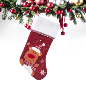Detail of red plush Christmas stocking with reindeer embroidery hanging on a festive tree
