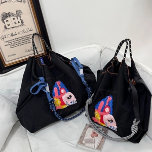 Detail of black nylon tote with 'Embrace Yourself' embroidery and woven rope handles