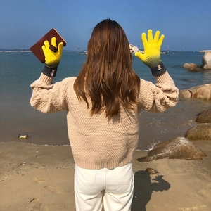 Detail of colorful gradient knitted touchscreen gloves worn against a scenic beach background