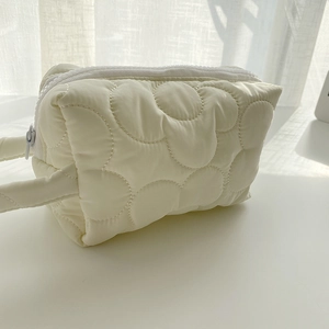 Detailed view of cream quilted makeup bag with circular stitching and a fabric handle