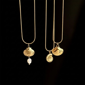 Gold shell and nautilus pendant necklaces with pearls on snake chains over black background