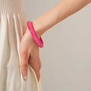 Detail shot of a bright pink translucent resin bangle worn on a model's wrist