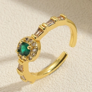 Detail of gold open ring with green round zircon and crystal accents on beige surface