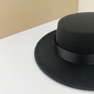 Close-up of the black wool felt flat top hat featuring a ribbed grosgrain ribbon band