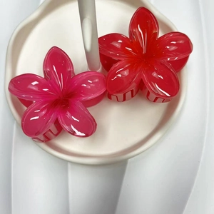 Detail view of two plumeria flower hair clips in translucent rose red and gradient red colors