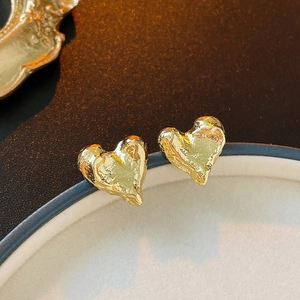Gros plan détaillé des boucles d'oreilles cœur dorées avec texture métal liquide et brillance
