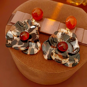 Detail of leopard print flower earrings with amber beads on a brown velvet surface