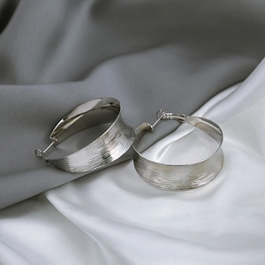 Macro detail of silver C-shaped hoop earrings with brushed metal texture on silk
