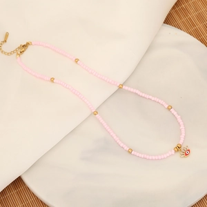 Detail of pink seed bead necklace with gold evil eye charm on white ceramic plate