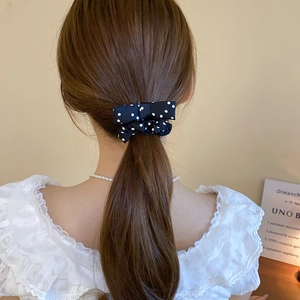 Close-up of a black and white polka dot satin bow hair tie worn on a ponytail