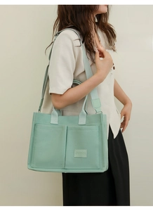 Close-up of a light green canvas tote bag with front pockets and crossbody strap on a model