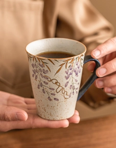 Detail of hand-painted wisteria ceramic mug with gold accents and a deep blue handle