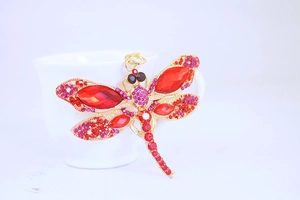 Detail of a dragonfly keychain with red crystals hanging on a white ceramic cup