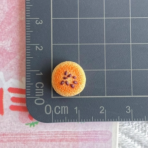 Detailed macro view of a 1.5cm miniature orange slice resin charm on a scale mat