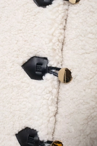 Dettaglio della giacca in pile crema con inserti in pelle nera e bottoni dorati