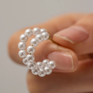 Close-up of C-shaped hoop earrings with multiple white pearls on a golden stainless steel post
