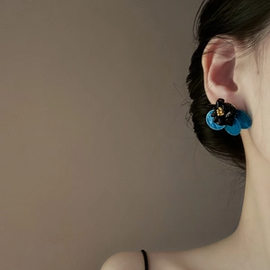 Close-up of a blue and black flower stud earring with gold accents on a female model