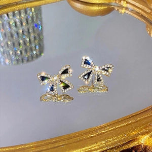 Macro shot of elegant black bow earrings with rhinestones on a golden mirror base