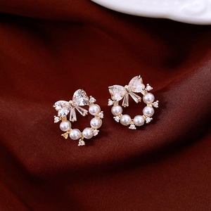 Close-up of bowknot pearl wreath earrings with zircon inlay on red velvet background