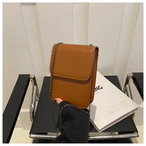 Detail of a minimalist brown leather mini crossbody phone bag with a sleek metal chain