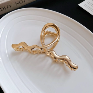Detail shot of wavy gold metal hair claw clip with glossy finish on a ceramic plate