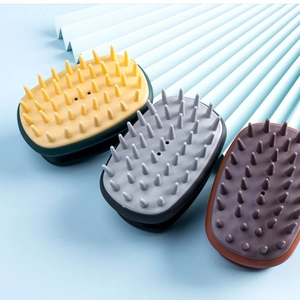 Three colorful silicone scalp massage brushes in yellow, grey, and reddish-brown on blue background