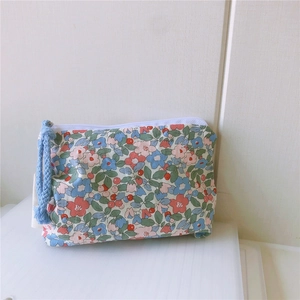 Detail of floral cotton mini pouch featuring a secure zipper and light blue woven tassel cord