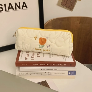 Detailed view of cream quilted tulip pencil case with orange floral embroidery on books