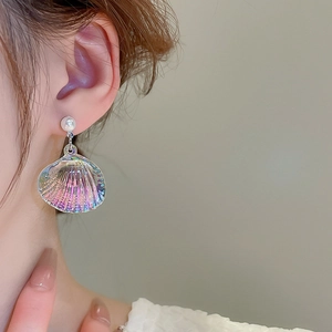 Detailed view of an iridescent shell earring with elegant pearl on a female model