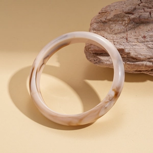 Détail d'un bracelet en acrylique crème avec texture marbrée contre une pierre naturelle