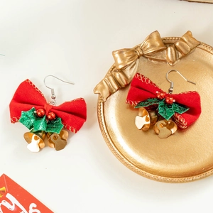 Boucles d'oreilles de Noël avec nœuds rouges, feuilles vertes et clochettes dorées sur plateau