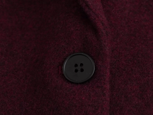 Macro shot of dark red wool fabric and a black four-hole button on the blazer sleeve