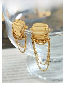 Detail of gold fringe earrings with layered chains hanging from a geometric square stud